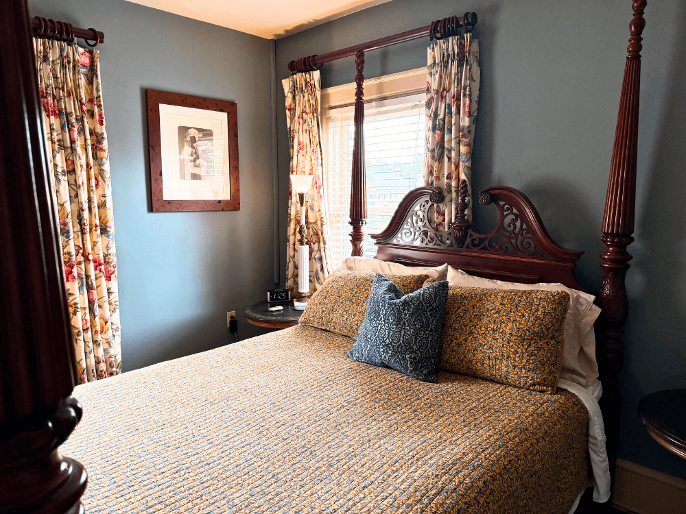 Cozy bedroom featuring a four-poster bed, floral curtains, and a decorative throw pillow.