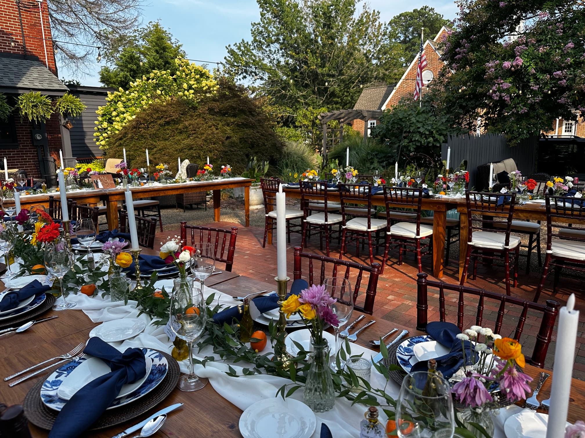 A beautifully arranged outdoor dining setup with decorated tables, fresh flowers, and elegant tableware amidst greenery.