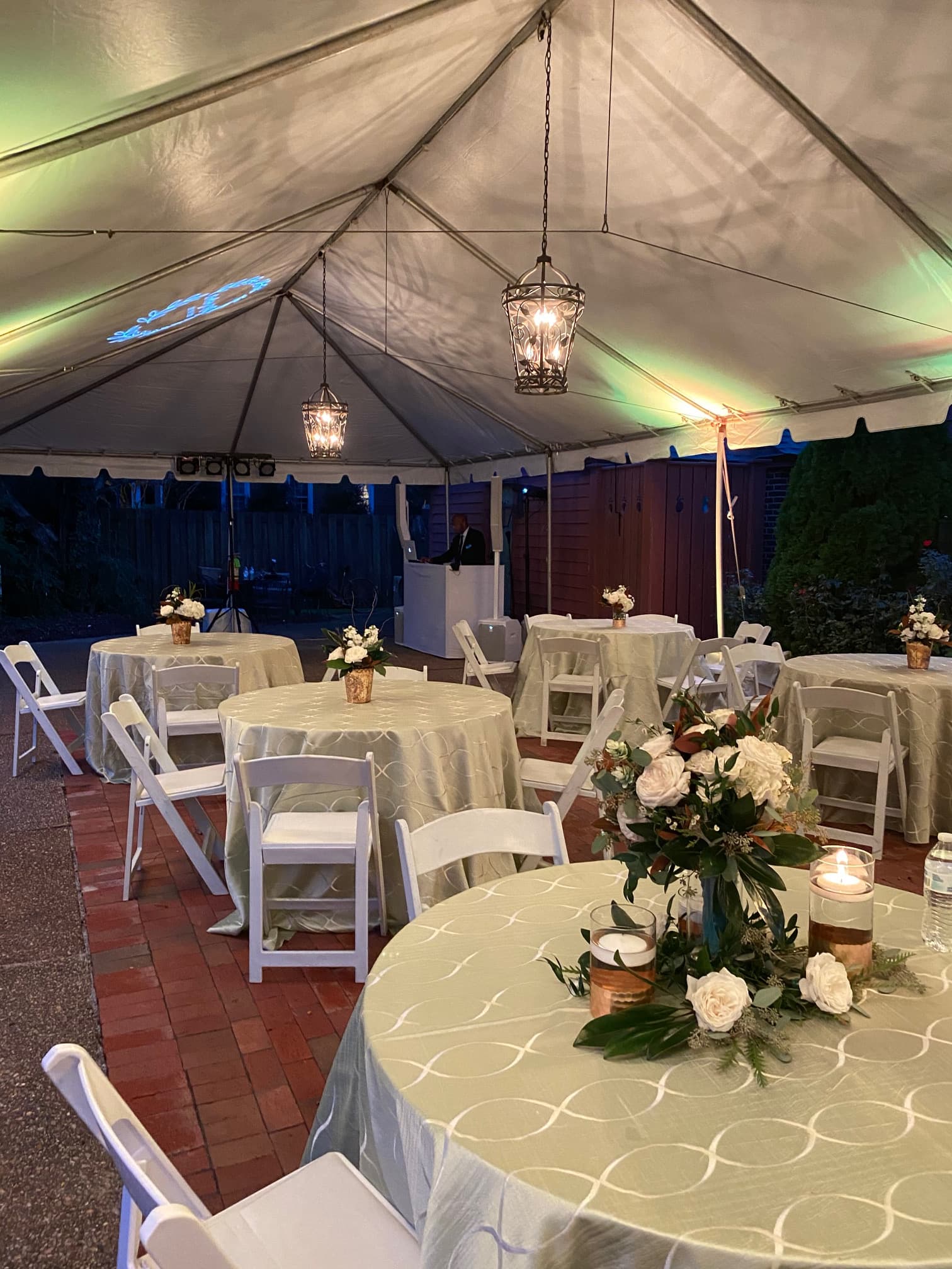 A beautifully decorated outdoor tent with tables set for an event, featuring floral centerpieces and elegant lighting.
