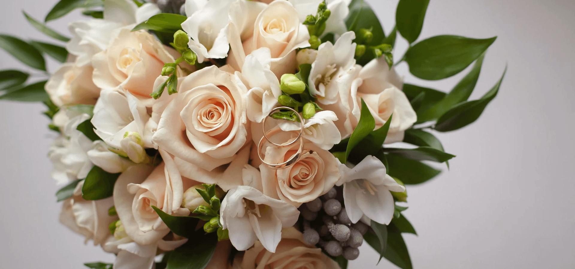 A bouquet of soft pink roses and white flowers with wedding rings intertwined among the blooms.
