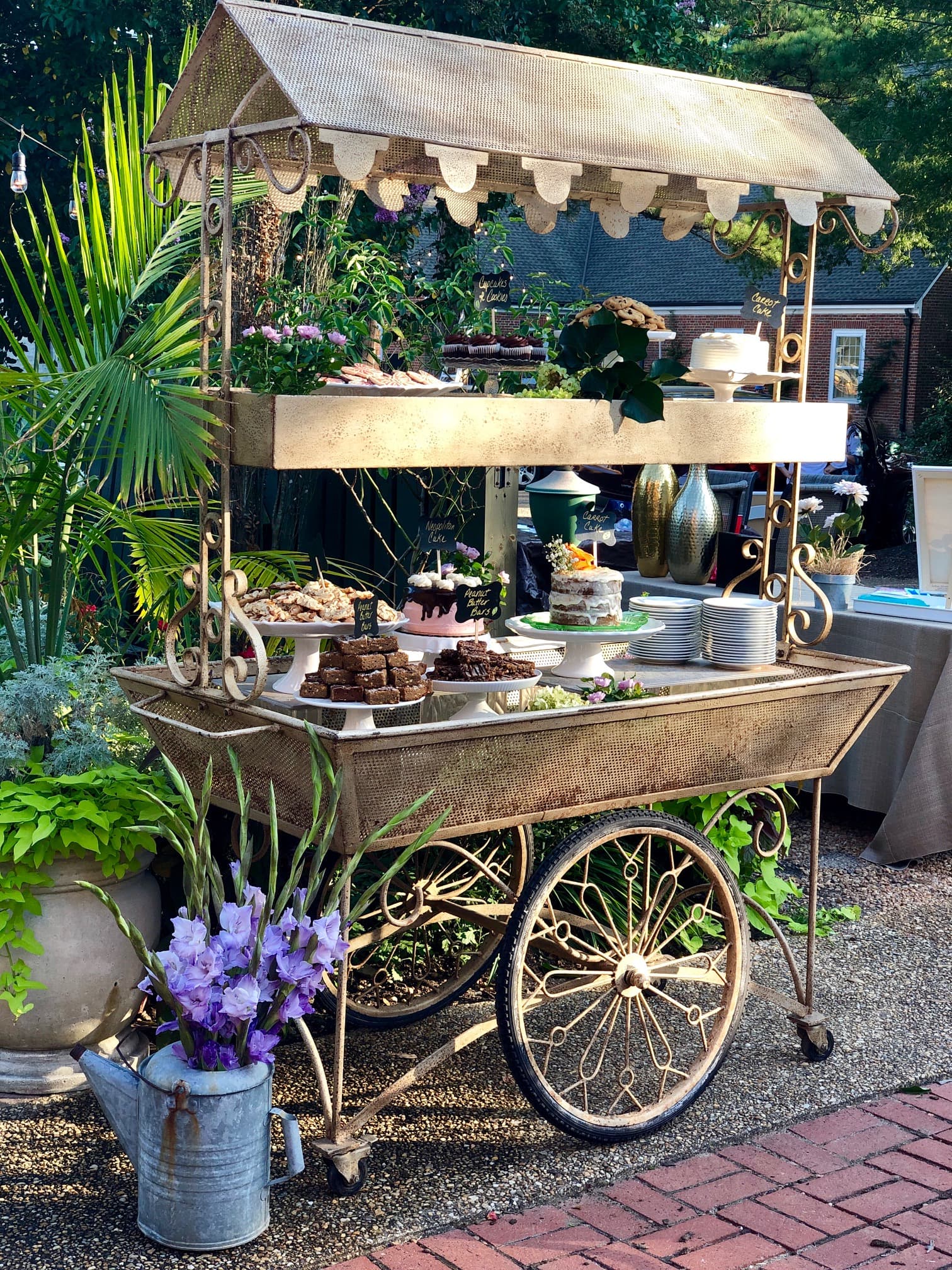 A vintage cart adorned with desserts and flowers in a decorative outdoor setting.