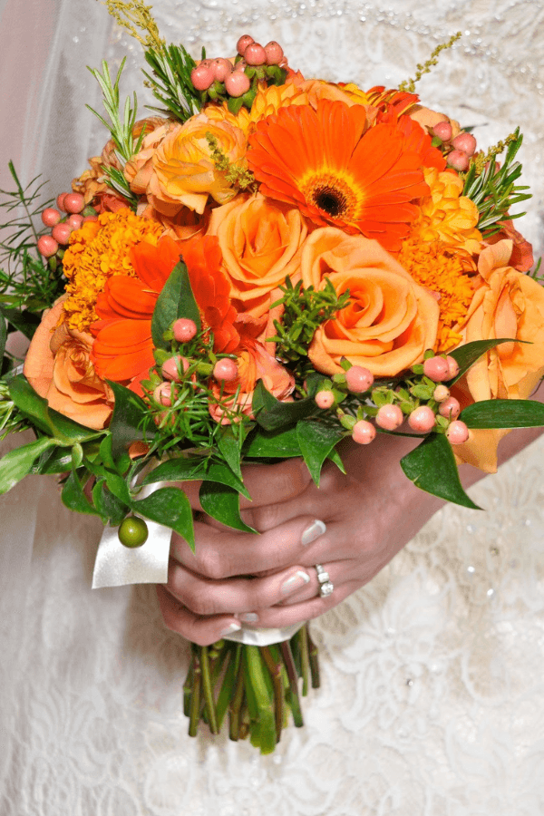 A close-up of a wedding bouquet featuring vibrant orange and peach flowers held by a bride.