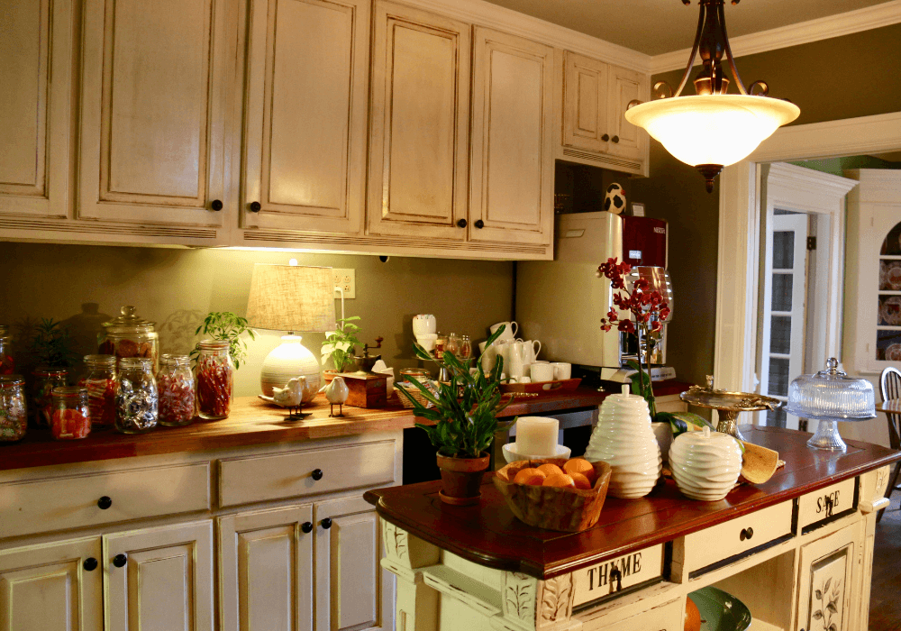 A cozy kitchen scene featuring a wooden countertop with potted plants, jars of colorful ingredients, and warm lighting.