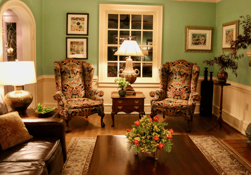 A cozy living room featuring two ornate armchairs, a decorative lamp, and a floral centerpiece on a coffee table.