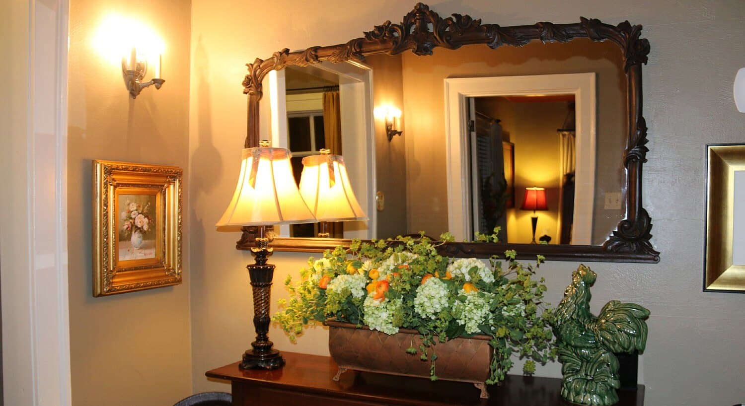 Dark wood entryway table with lamp, large ornate mirror, and decorative flowers