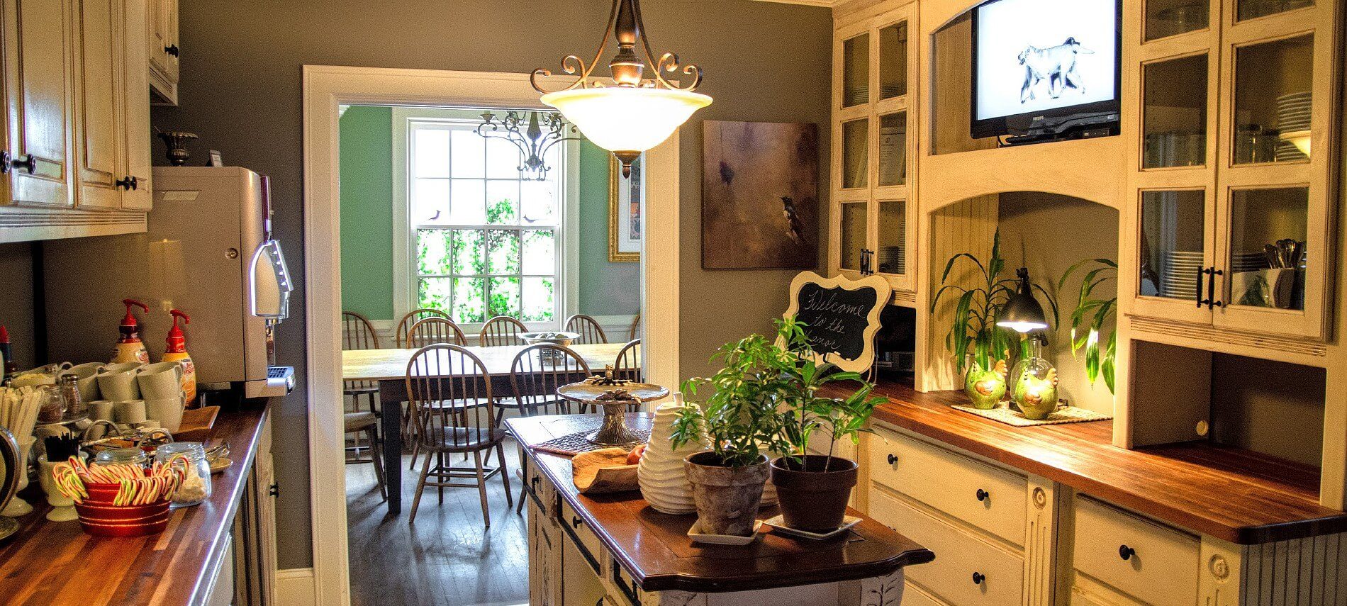 Large white kitchen with brown countertops displaying coffee cups and decorative pieces and doorway into a dining room