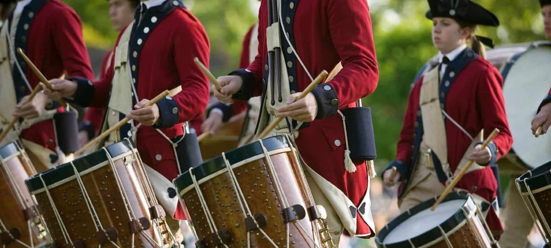 Group of young people in colonial costumes marching as they beat on drums