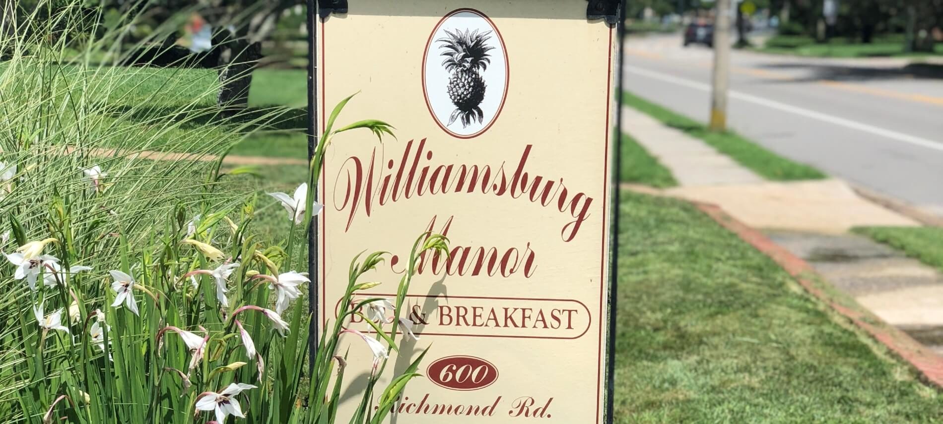 Vertical rectangular yellow sign with business name in cursive red lettering on a green lawn by white flowers