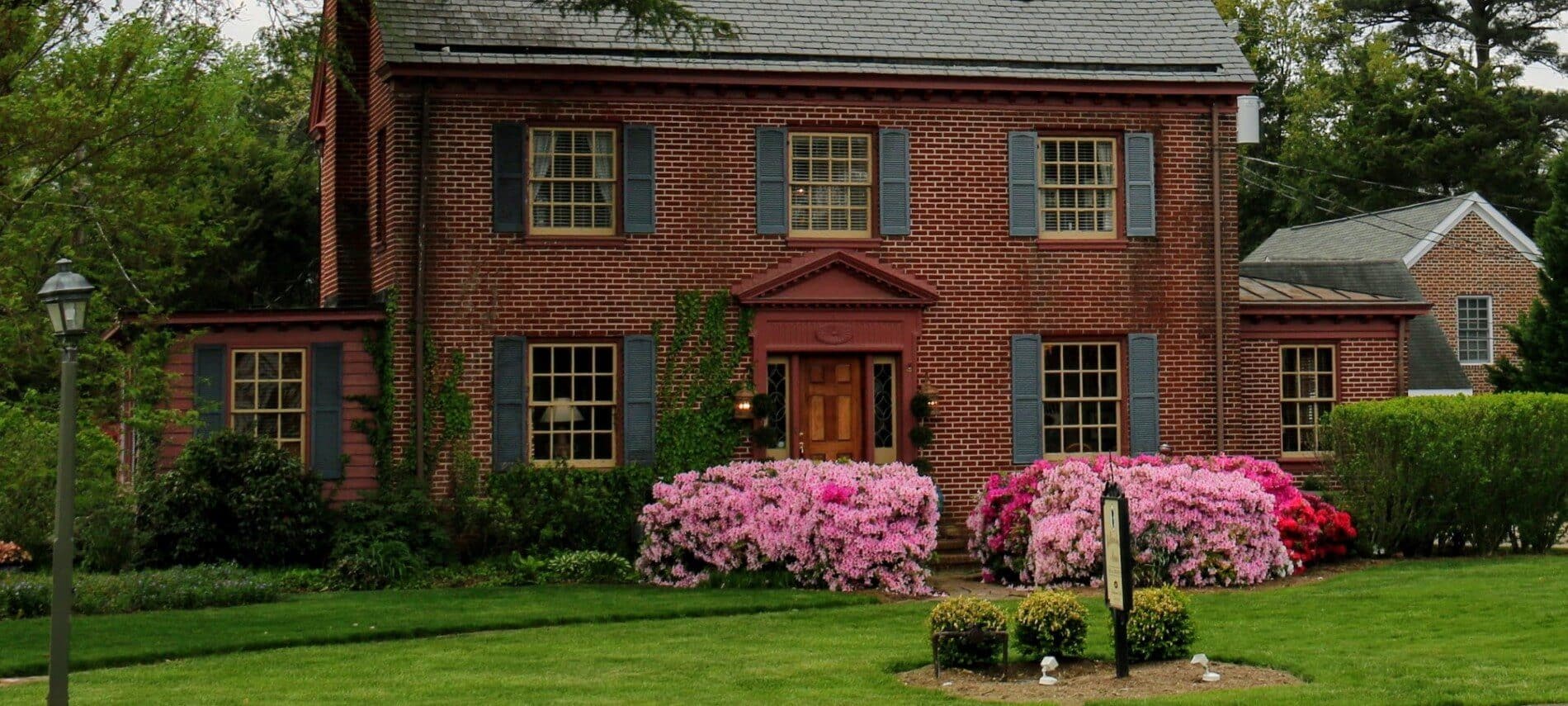 Front facade of an elegant red brick home with several windows and tall pink flowering shrubs by the front path