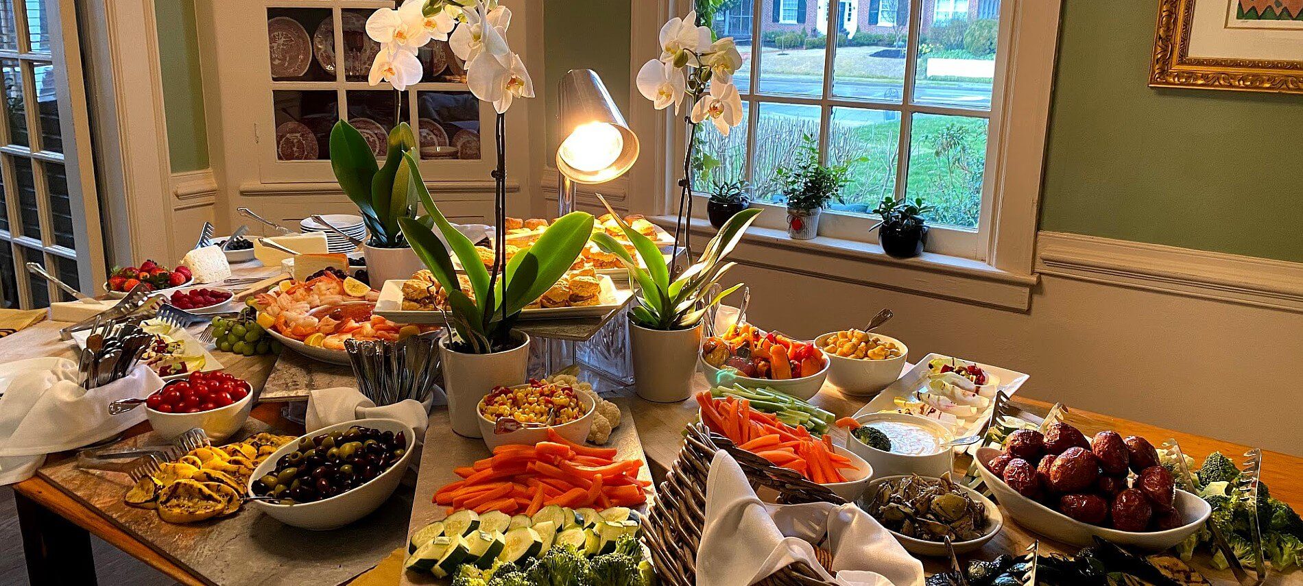 Large table beautifully displaying a colorful variety of vegetables, shrimp, fruits and cold dishes with tall white flowers as centerpieces