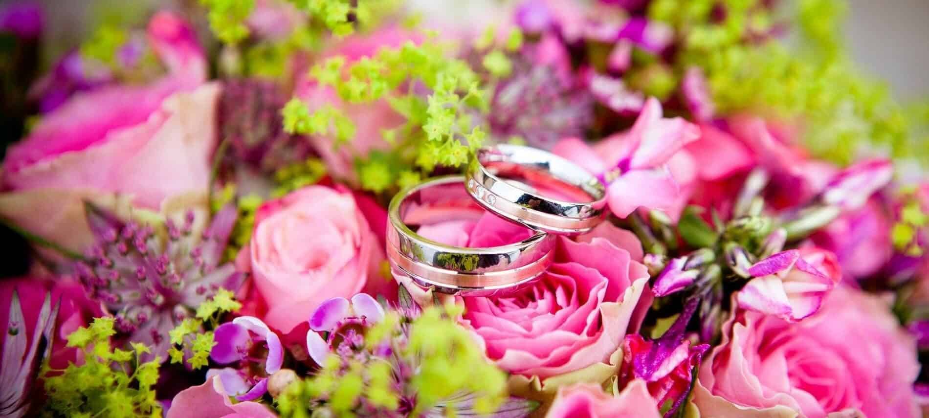 Gorgeous array of pink and purple flowers with an up close view of two silver wedding bands sitting on top