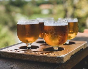 Wooden platter featuring a flight of four short glasses of light colored beer