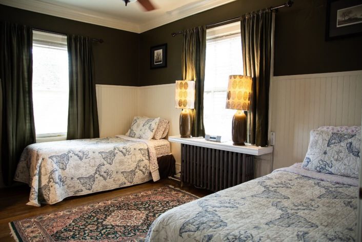 Two twin beds in guest room with black and white walls, large window and oriental rug on the floor