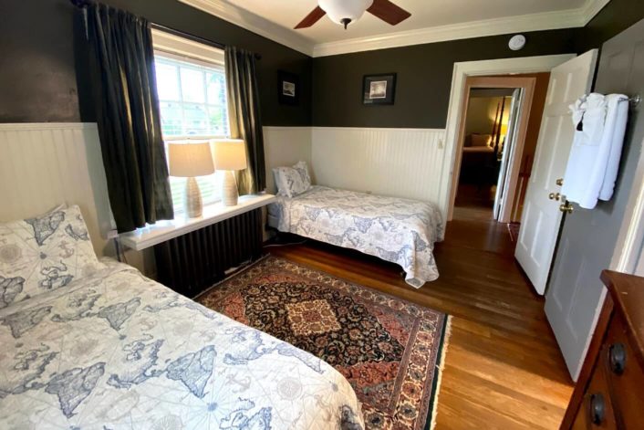 Guest room with two twin beds in front of large window with oriental rug on the floor and doorway into second bedroom