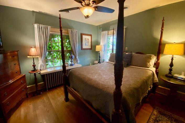 Four poster bed in luxurious guest room with green walls, brown accent furniture and large bright windows