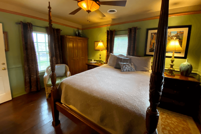 Spacious guest room with dark brown four poster bed, side tables with lamps, armoire and paintings on the wall