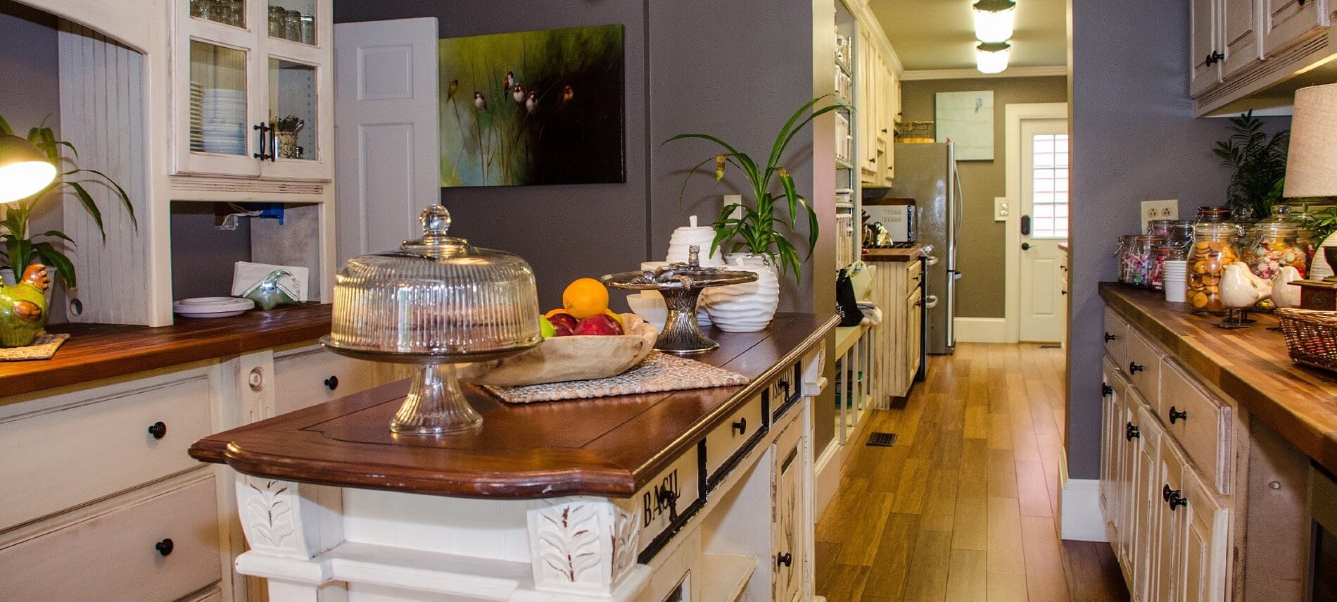 Large galley kitchen with white cabinets, dark wood countertops, island and several food dishes and jars of candy