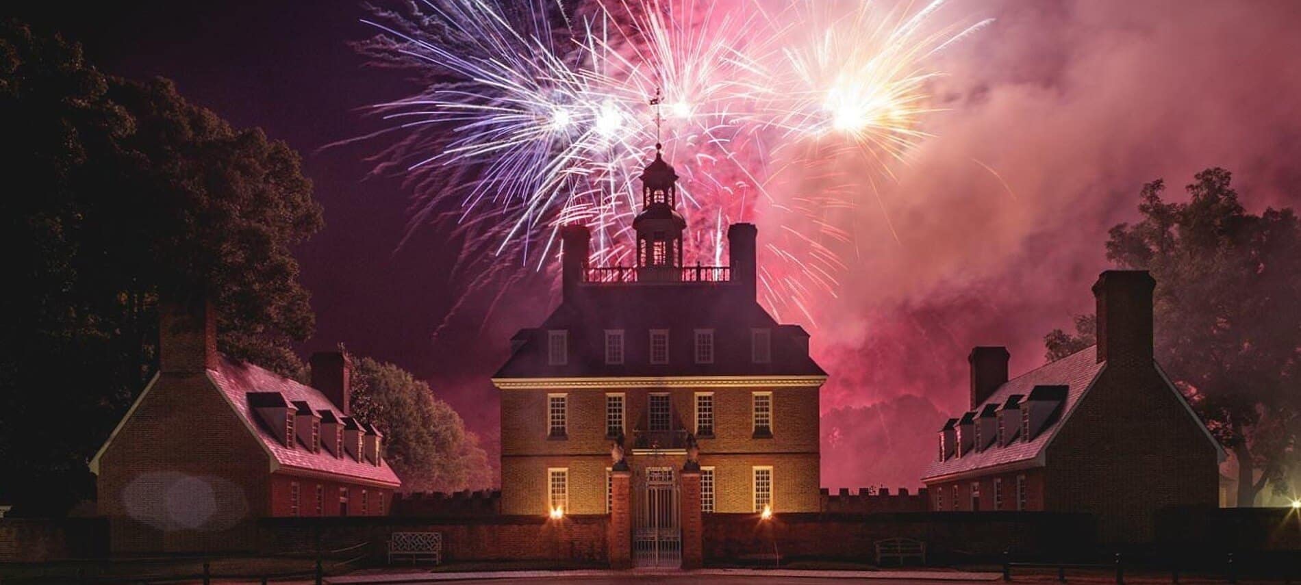 Night sky lit up pink and purple from fireworks over stately brick historic establishment