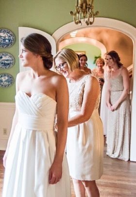 Mother of the bride attending to a bride's dress while bridesmaids look on in the background